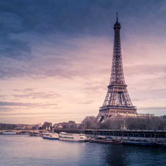 A beautiful wide shot of Eiffel Tower in Paris surrounded by water with ships under the colorful sky